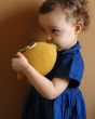 Girl stood in front of a beige wall cuddling the Myum handmade crochet lemon toy