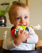 A child happily grasping and chewing on the Sophie The Giraffe - Nature Chew Rattle