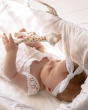 A child laid in a baby basket, looking up and holding the Sophie la Girafe natural rubber teether