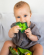 Young child sat down holding the Oli & Carol natural rubber kale baby teething toy in its mouth