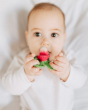 Close up of a baby chewing on the oli and carol eco-friendly radish teether on a white bed