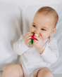 Close up of a baby chewing the oli and carol natural rubber soft baby teething toy on a white bed