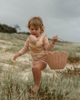 Child wearing the Dinkum Doll Gumdrop carrier on their front holding a dozy dinkum doll, the child is holding a basket, walking through the grass