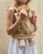 Child wearing the Dinkum Doll Gumdrop carrier on their front holding a  dinkum doll and a small pink flower