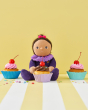 Freya Fondant is sat between delicious cupcakes, on a yellow and white stripe background