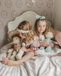 2 young girls sat on a bed playing with some Olli Ella dinkum dolls in the vintage floral and boar print pyjamas