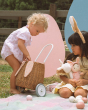 Two children playing outside in the sun. One child is looking into the Olli Ella Rattan Bunny Luggy with Lining – Gumdrop, the other is holding various Olli Ella dolls