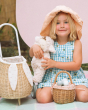 A child smiling and holding an Olli Ella Lamby Doll. In front of the child is an Olli Ella Rattan Lined Basket in Gumdrop, and an Olli Ella Rattan Bunny Luggy with Lining – Pansy Floral