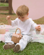 A child sat on a colourful basket, happily playing with the Olli Ella Rattan Berry Basket with Lining – Gumdrop. A beautiful lined rattan basket, with gumdrop print on a cream background