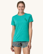 An adult wearing the Patagonia Women's Capilene Cool Daily Graphic Shirt - Trail Trotters / Subtidal Blue X-Dye, showing a patagonia running footprint logo on the front of the t-shirt, on a cream background