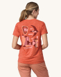 An adult showing the swift flying over a colourful rock formation on the back of the Patagonia Women's Capilene Cool Daily Graphic Shirt - Granite Swift / Pimento Red X-Dye, on a cream background