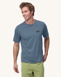 An adult wearing the Patagonia Men's Capilene Cool Daily Graphic Shirt - 73 Skyline / Utility Blue X-Dye, with a black Patagonia mountain logo on the front of the t-shirt, with light green shorts. This photo also shows the fit on the front of the t-shirt