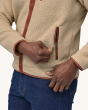 An adult wearing a Patagonia Men's Retro Pile Jacket showing the zipper, and brown zipper pulls, with denim blue jeans