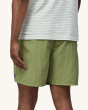A person wearing Patagonia Men's Baggies Beach Shorts - Buckhorn Green, with a white  and thin green stripe t-shirt showing the fit of the shorts from the back