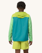 A person wearing Patagonia Men's Baggies Beach Shorts - Phosphorus Green, and a lightweight yellow, blue and light green pull over jacket, showing the fit of the shorts from the back
