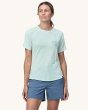 An adult wearing the Patagonia Women's Capilene Cool Trail Graphic Shirt - Forge Mark Crest / Wispy Green, with a black Patagonia Built to Endure logo on the front of the top, and light grey/blue shorts. This photo shows the fit of the top from the front