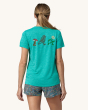 An adult wearing the Patagonia Women's Capilene Cool Daily Graphic Shirt - Trail Trotters / Subtidal Blue X-Dye, showing a patagonia running logo of a flower, mushroom and tree on the back of the t-shirt, on a cream background.