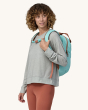 An adult wearing the Patagonia Atom Tote Backpack 20L - Skiff Blue, showing the chest strap on the front, on a cream background