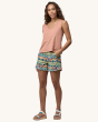 An adult wearing the Patagonia Women's Baggies Shorts - High Hopes Geo / Salamander Green with a peach coloured top and white sandles, on a cream background