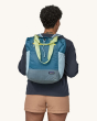 The front of the Patagonia Ultralight Black Hole Tote Pack on an adults back. Image is a blue backpack with lime green carry straps and a yellow zipper