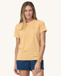 An adult wearing the Patagonia Women's Capilene Cool Daily Graphic Shirt - Boardshort Logo / Sandy Melon X-Dye, with silver Patagonia writing on the front of the t-shirt, and wearing navy blue shorts