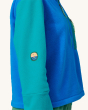 An adult wearing a Patagonia Women's Microdini 1/2 Zip Fleece Pullover, showing a close up of the Patagonia Sun and Earth logo on the elbow of the fleece. Fleece is in Vessel Blue