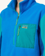 An adult wearing a Patagonia Women's Microdini 1/2 Zip Fleece Pullover, showing a close up of the pocket and zips. Fleece is in Vessel Blue