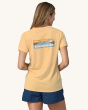 An adult wearing the Patagonia Women's Capilene Cool Daily Graphic Shirt - Boardshort Logo / Sandy Melon X-Dye, with a Patagonia wave logo on the back of the t-shirt, and wearing navy blue shorts