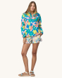 An adult wearing the Patagonia Women's Lightweight Synchilla Snap-T Fleece Pullover - Channeling Spring / Natural, with colourful shorts and sandles, on a cream background. This fleece has bright, colourful flower print details in pink, green, yellow and 