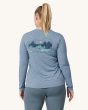An adult wearing a Patagonia Women's Long-Sleeved Capilene Cool Daily Graphic Shirt, showing the fit of the top from the back and wearing light grey leggings