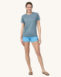 An adult wearing a The Patagonia Women's Capilene Cool Daily Graphic Shirt showing the fit of the t-shirt, and light blue shorts