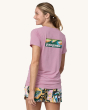 An adult wearing the The Patagonia Women's Capilene Cool Daily Graphic Shirt - Boardshort Logo / Milkweed Mauve X-Dye, showing the Patagonia wave logo on the back of the t-shirt, and colourful tropical shorts