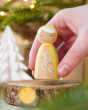 Close up of a hand holding a Peepul Mistletoe handmade wooden peg doll toy over a wooden log