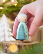 Close up of a hand holding a Peepul Winter Berries handmade wooden peg doll toy over a wooden log