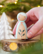 Close up of a hand holding a Peepul Holly handmade wooden peg doll toy over a wooden log