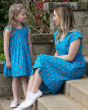 Woman and young girl sat on some stone steps wearing matching Piccalilly blue parrot wrap dresses 