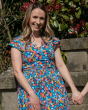 Woman leaning against a stone wall wearing the Piccalilly organic cotton tropical wrap dress