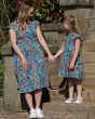 Woman and young girl stood on some steps wearing matching Piccalilly organic cotton wrap dresses in a multicoloured tropical print
