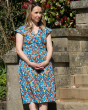 Woman leaning against a stone wall wearing a multicoloured Piccalilly organic cotton wrap dress
