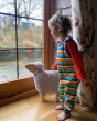 Child stood in front of a large window wearing the Piccalily eco-friendly rainbow stripe dungarees