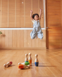 Close up of the PlanToys plastic-free bowling pins scattered on a wooden floor in front of a child, jumping in the air and celebrating