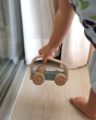 Close up of a childs hand picking up the Plan Toys eco-friendly vroom car pushing toy on a light wooden floor