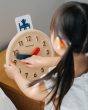 Close up of young girl turning the hands on the PlanToys plastic-free wooden activity clock 