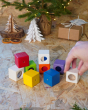 Close up of hand grabbing a white block from the PlanToys kids wooden sensory activity blocks in front of a small Christmas tree