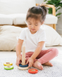 Child sat on a white carpet playing with the PlanToys plastic-free wooden sorting and stacking game