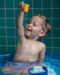 Close up of a young boy playing with pieces of the PlanToys solid wooden tugboat toy in a paddling pool