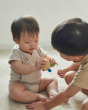Close up of two young children sat on the floor looking at the PlanToys multicoloured flexi jellyfish baby toy