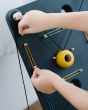 Close up of a child's hands pulling on a rubber band to attach to the PlanToys wooden wall ball game