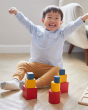 Young child sat on the floor cheering, next to 3 stacks of PlanToys matching and nesting blocks
