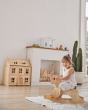 Young girl sat on a PlanToys wooden rocking horse on a white rug in front of a Victorian dollhouse toy
